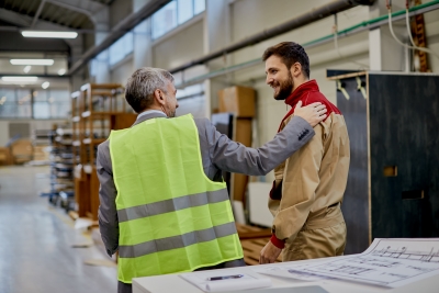 Happy factory worker communicating with company manager at woodworking industrial facility.