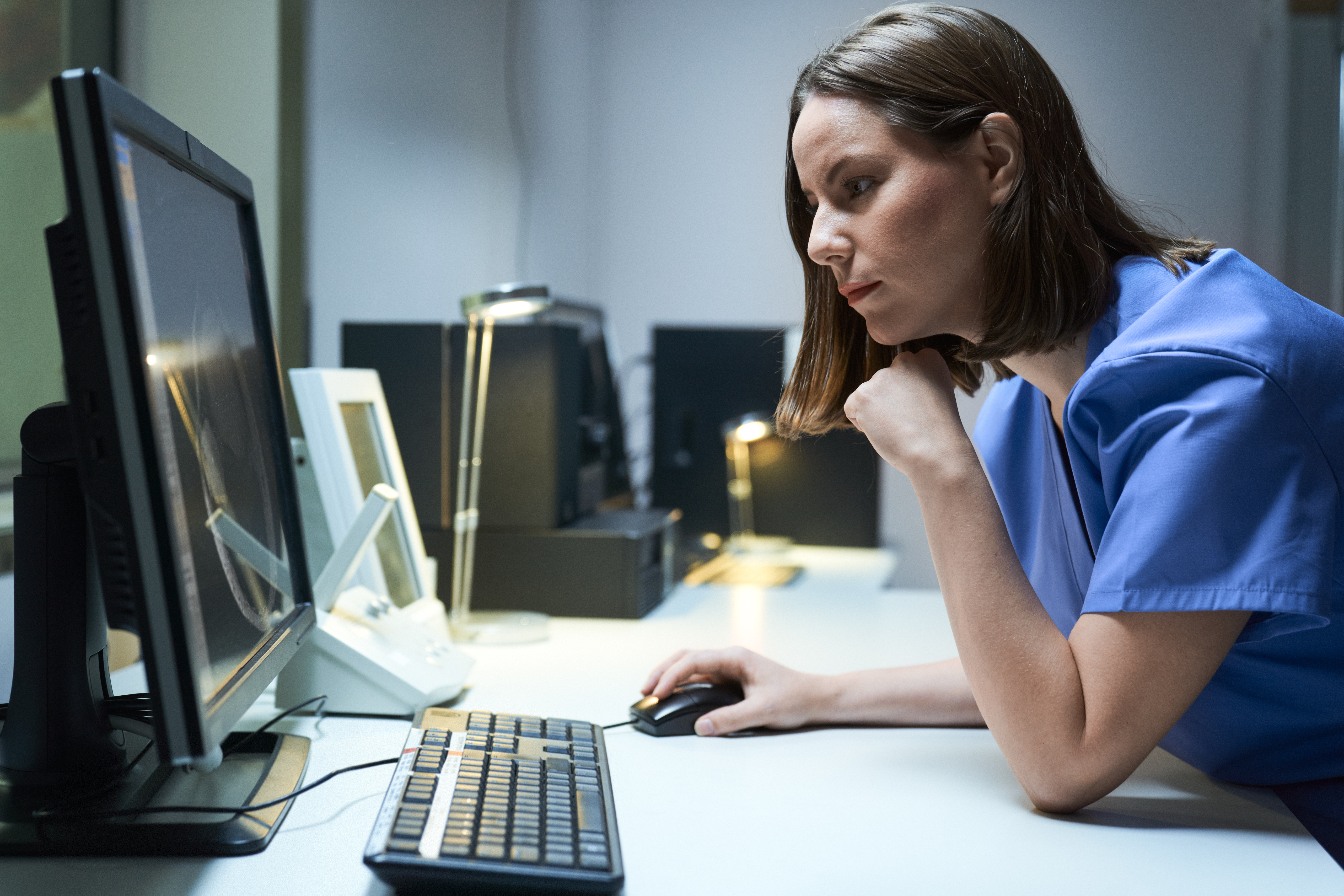 Healthcare worker looking closely at computer in dark room