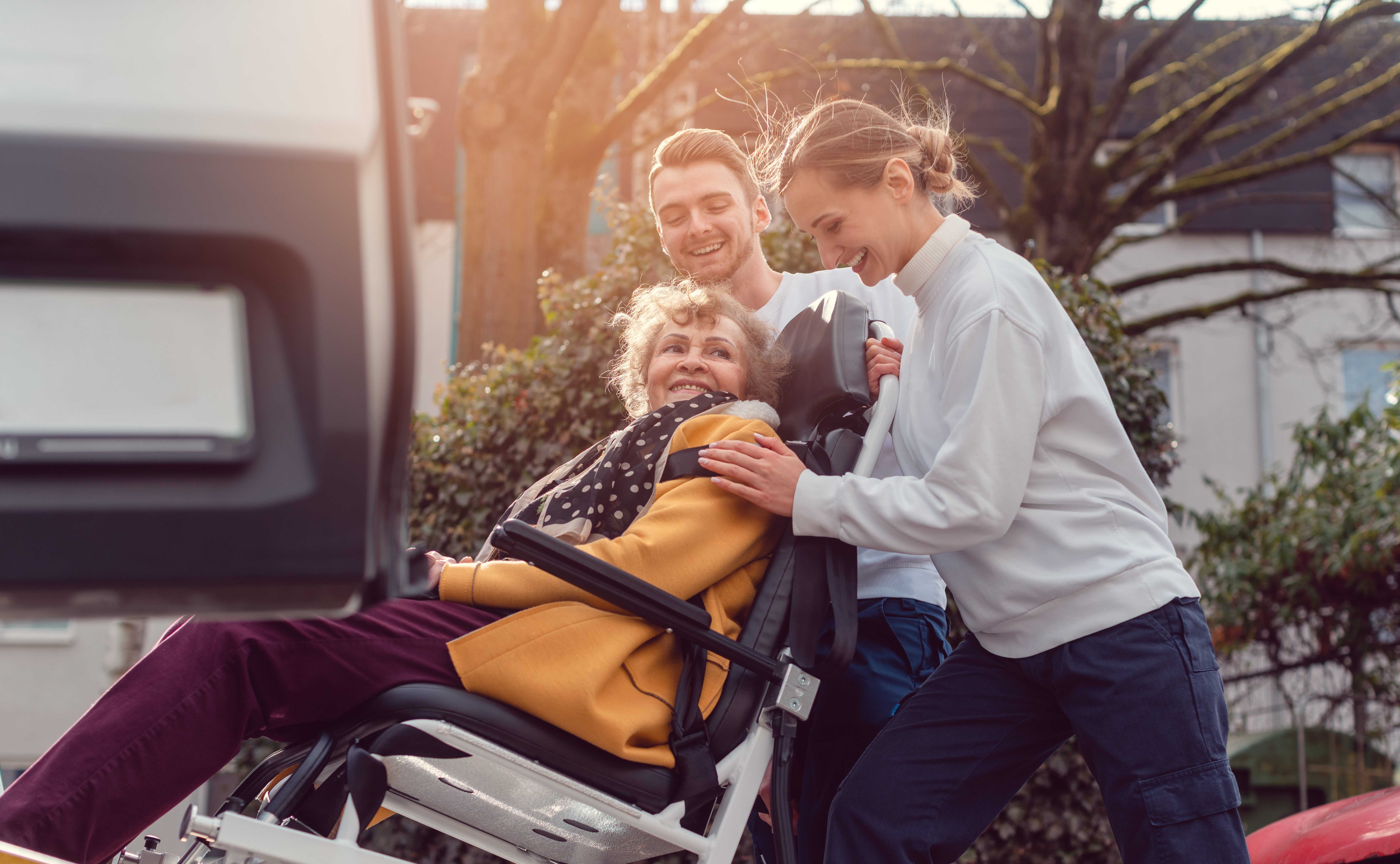 Two people helping push older woman in wheelchair