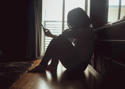 woman sitting in dark looking at phone sad