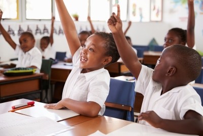 young black students raising hands in classroom
